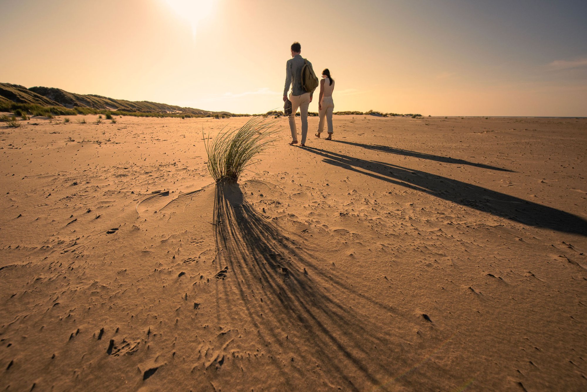Koppel wandelt over het strand bij zonsondergang op Terschelling, omringd door duinen en zacht avondlicht – symbool voor rust, natuur en luxe verblijf bij Elements by Dutchen.