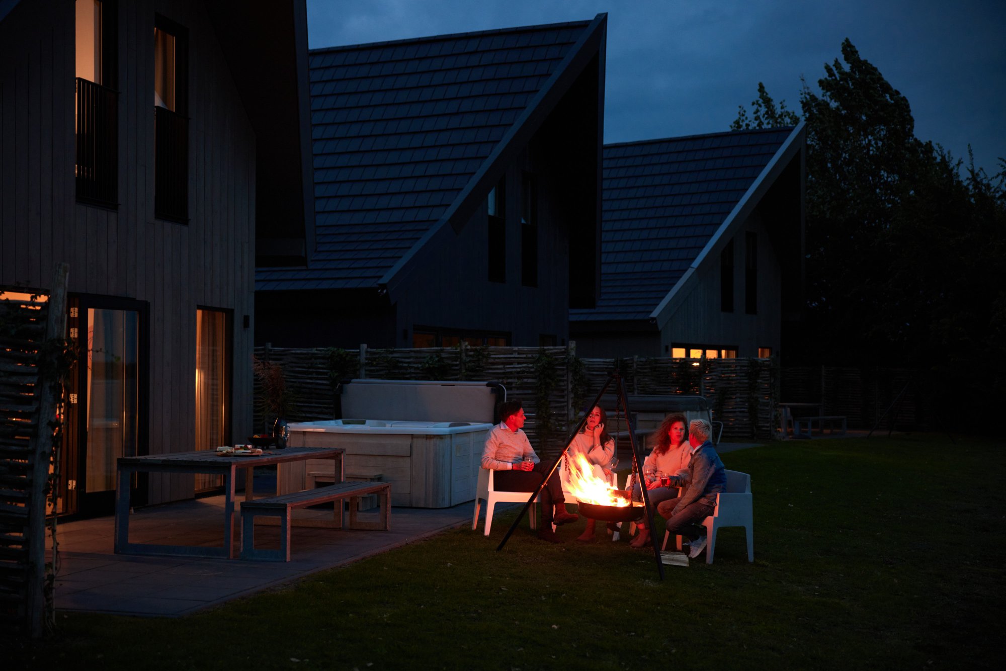 Gasten bij de vuurkorf naast een vakantiehuis met whirlpool in de avond.