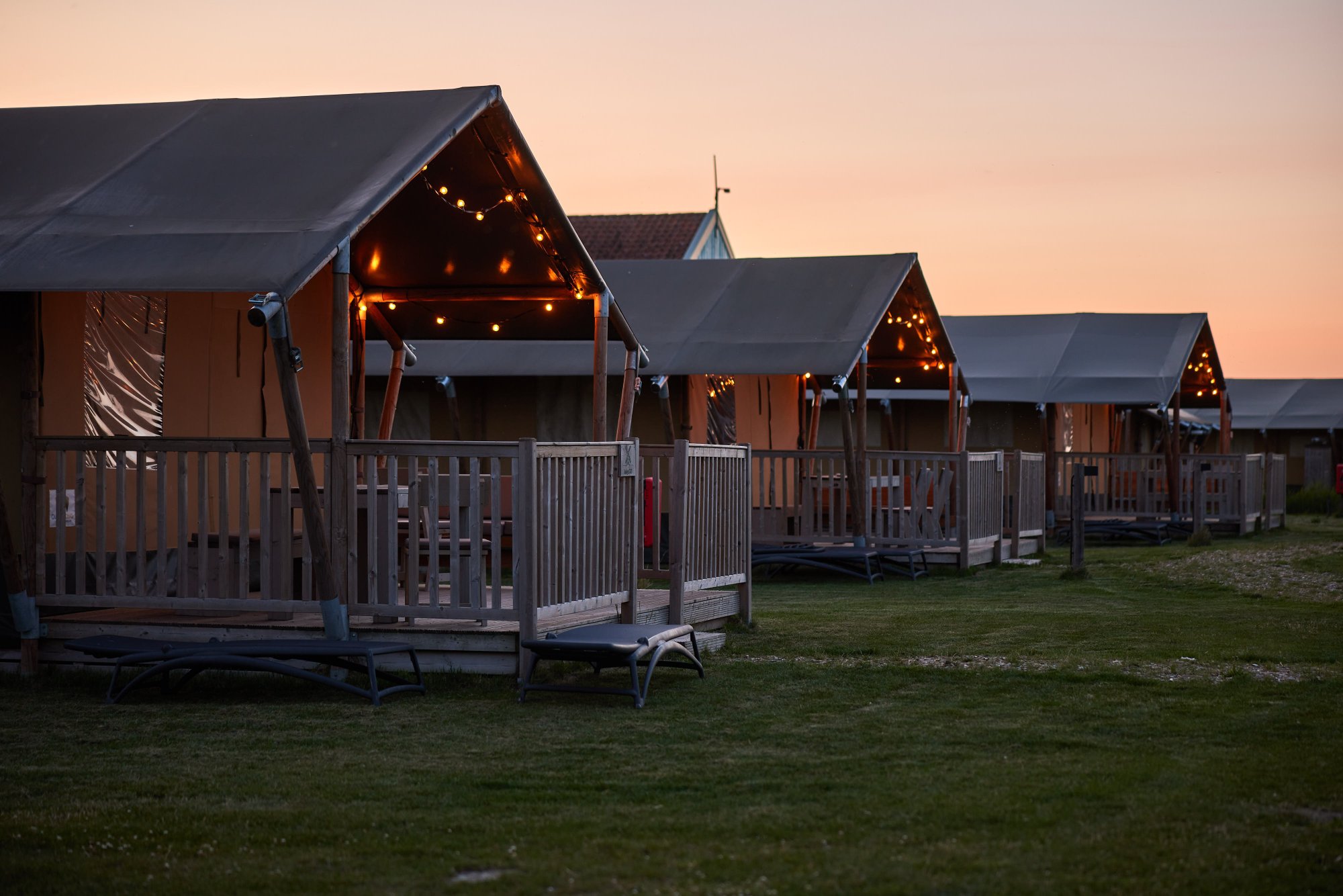 Lodgetenten op Erfgoedpark De Hoop met sfeerverlichting in de avond.
