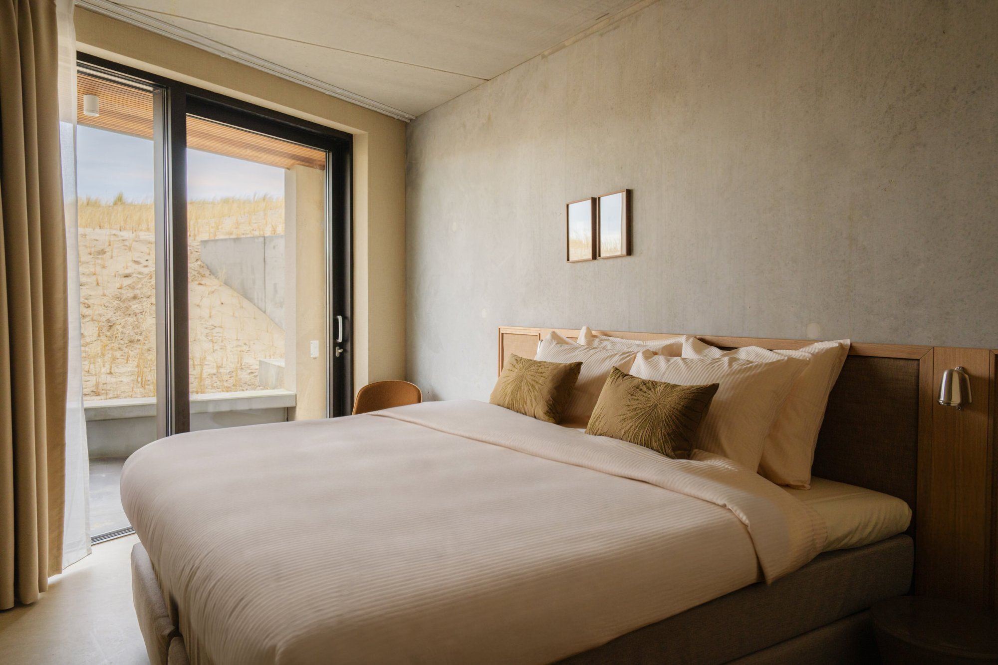 Slaapkamer met groot raam en uitzicht op de duinen.