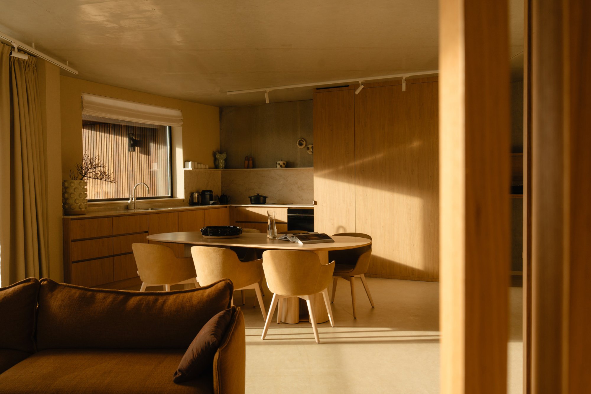 Warme, modern ingerichte keuken en eethoek in een Duinzicht appartement op Terschelling, met houten keukenkasten, ronde eettafel en zacht avondlicht dat door het raam naar binnen valt.