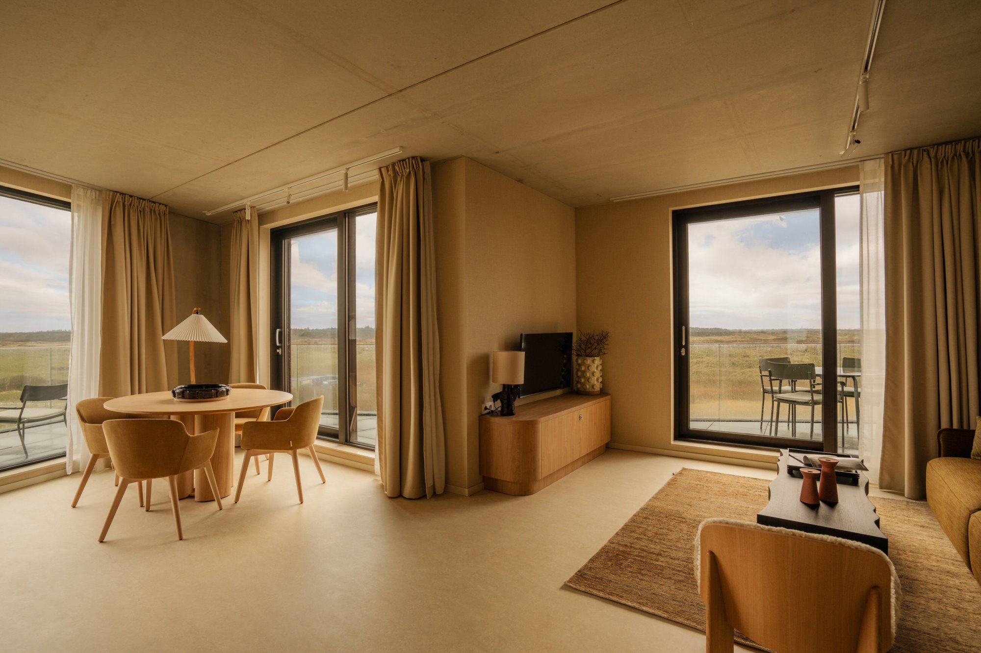 Ruime woonkamer van een luxe appartement op Terschelling met eethoek, grote ramen en uitzicht op de duinen.