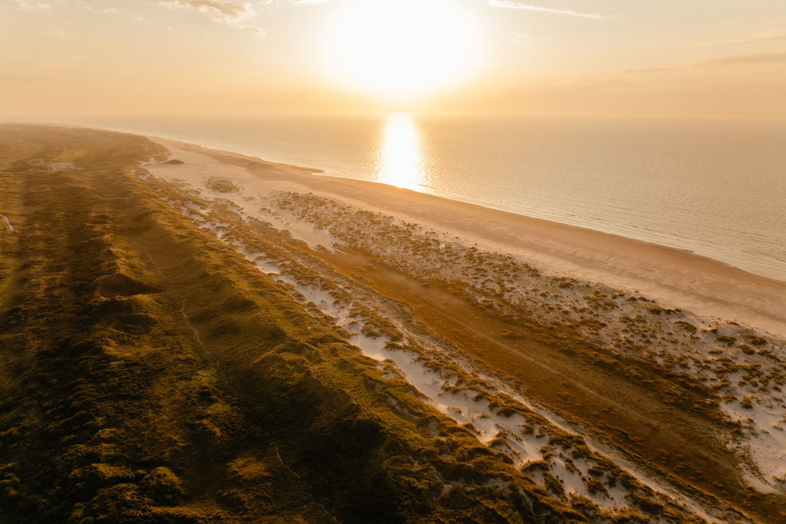 Zonsondergang boven de duinen en het strand van Terschelling, met warm goud licht over zee en zand.