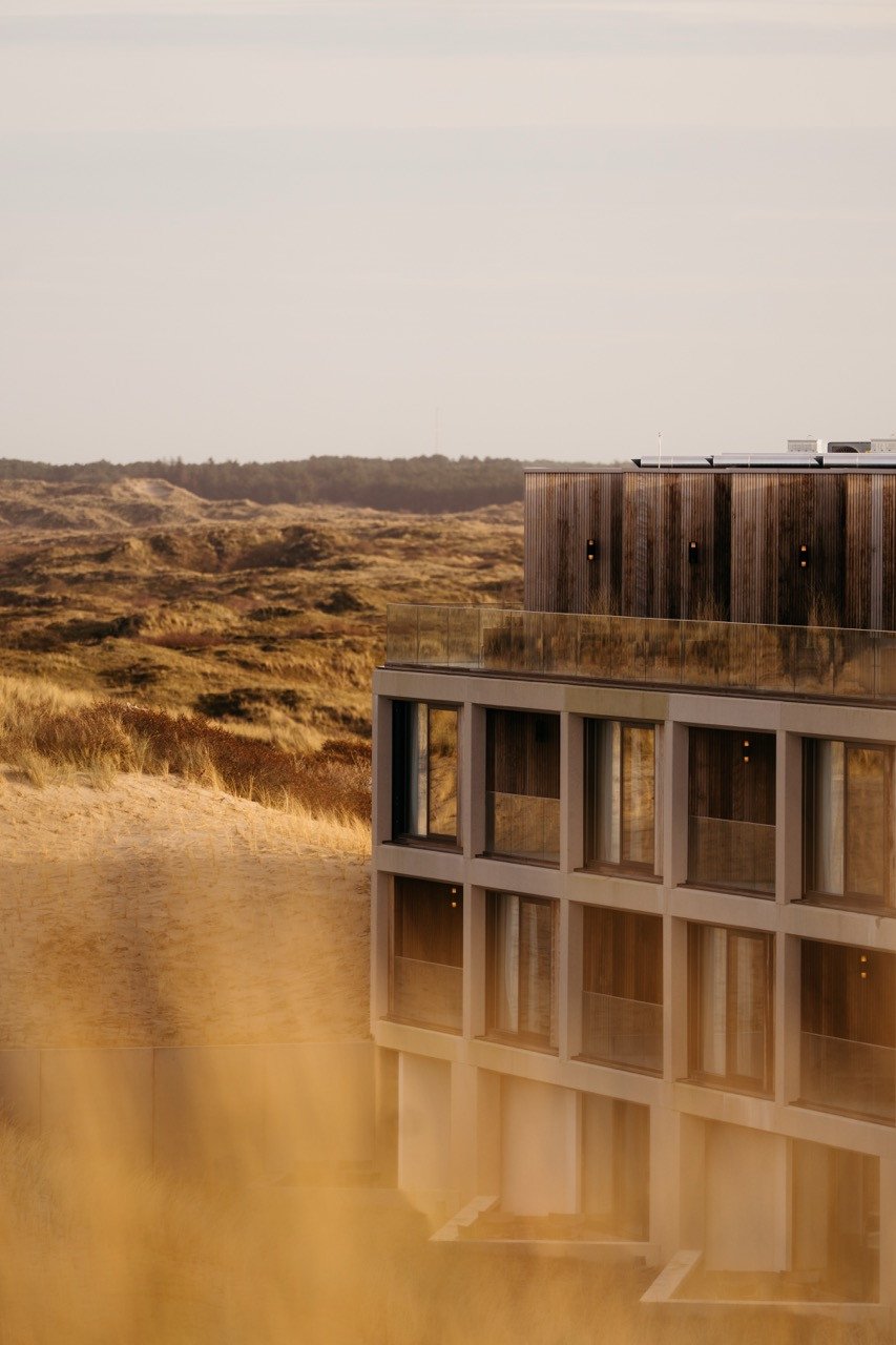 Exterieur beeld van Elements Terschelling met grote ramen en een houten bovenverdieping, midden in de duinen.