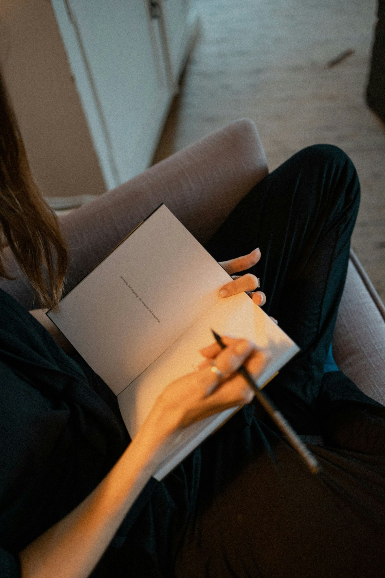 Vrouw zit in een fauteuil met een opengeslagen notitieboek op schoot en een pen in haar hand.