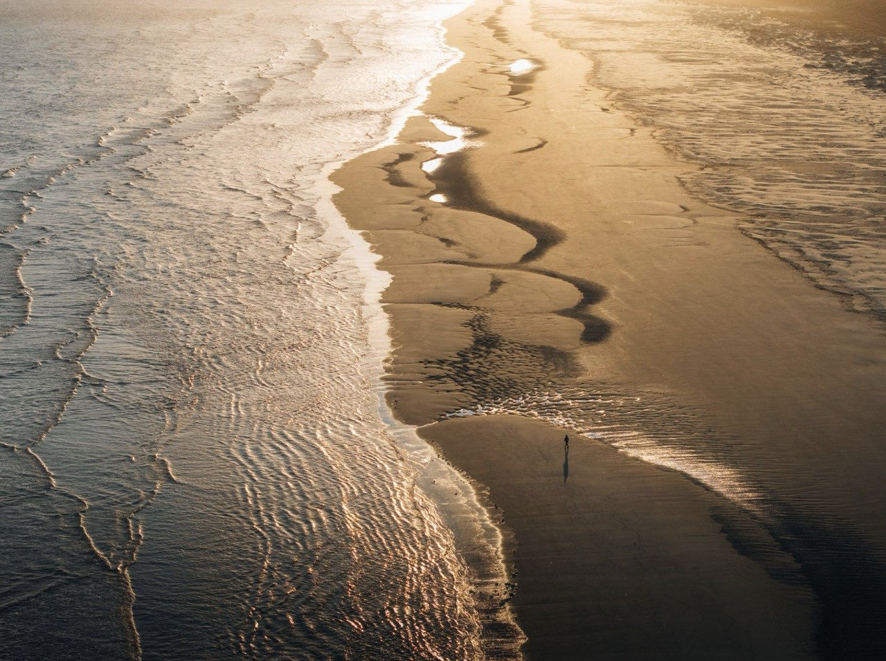 En prachtig dronebeeld van de branding van het Noordzeestrand van Terschelling. De afdrukken van de zee in het stand en de golven in de branding. In het mooiste moment van de dag, het gouden uur - wanneer de zon wat lager aan de hemel staat.