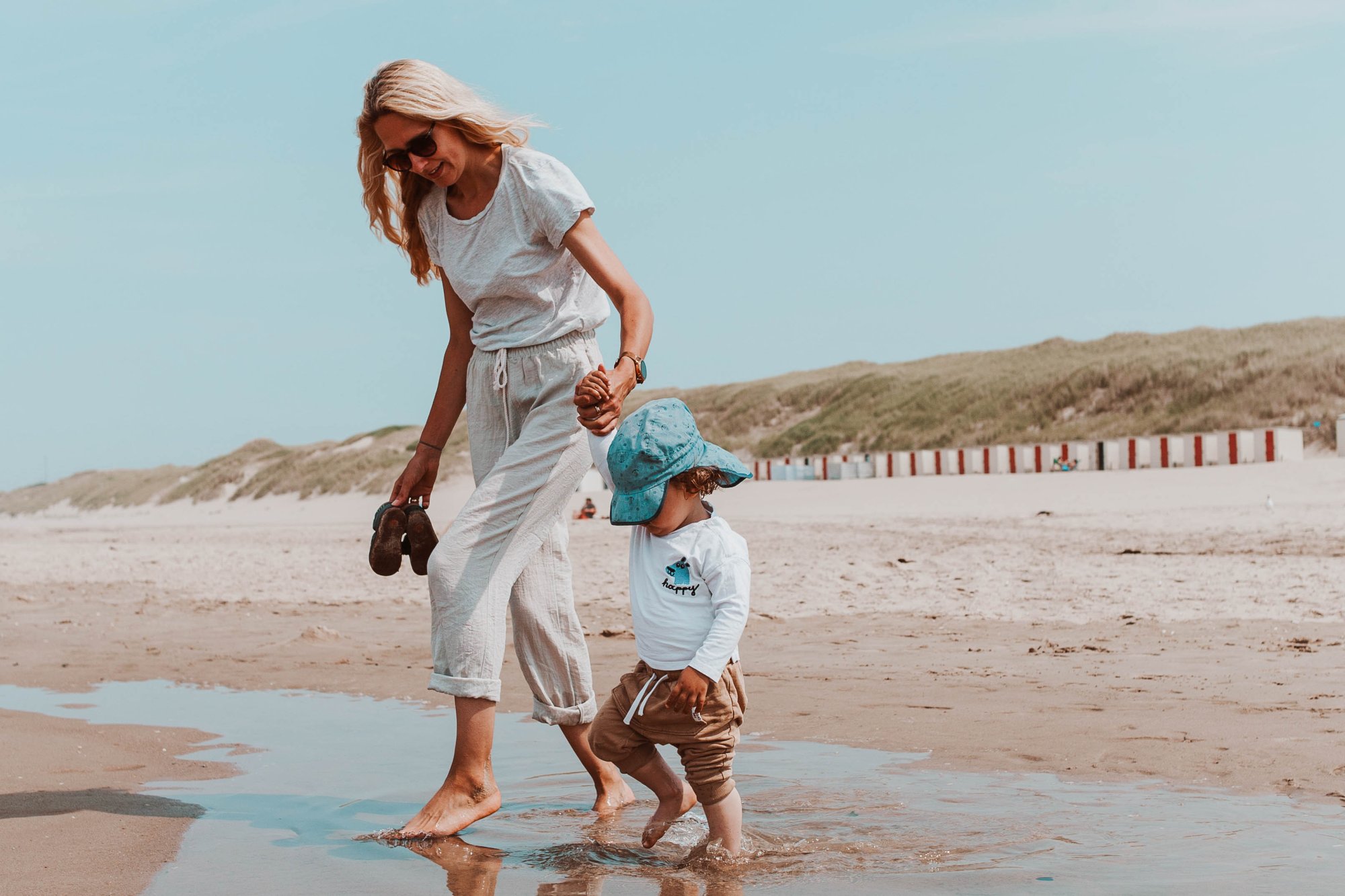 Moeder wandelt hand in hand met haar kind door het ondiepe zeewater op het strand bij Schoorl.