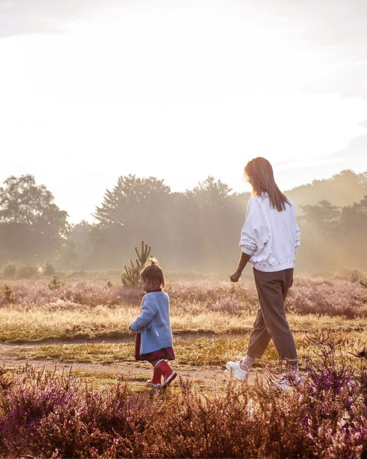 Moeder en kind wandelen door de bloeiende heidevelden in de Gooilanden tijdens een zonnige ochtend.