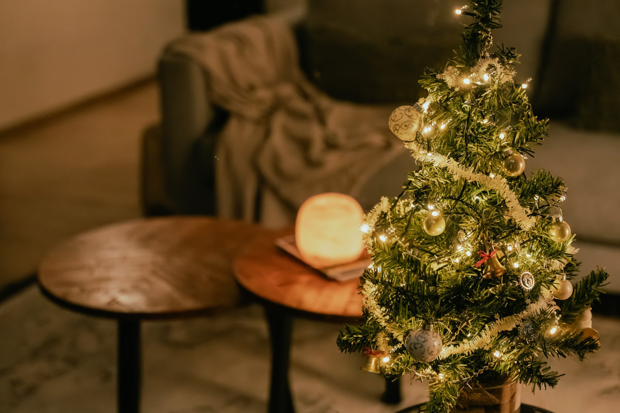 Sfeervol verlicht kerstboompje in een knusse zithoek, met warme accenten en een plaid op de achtergrond – perfect voor een ontspannen feestdagenverblijf.
