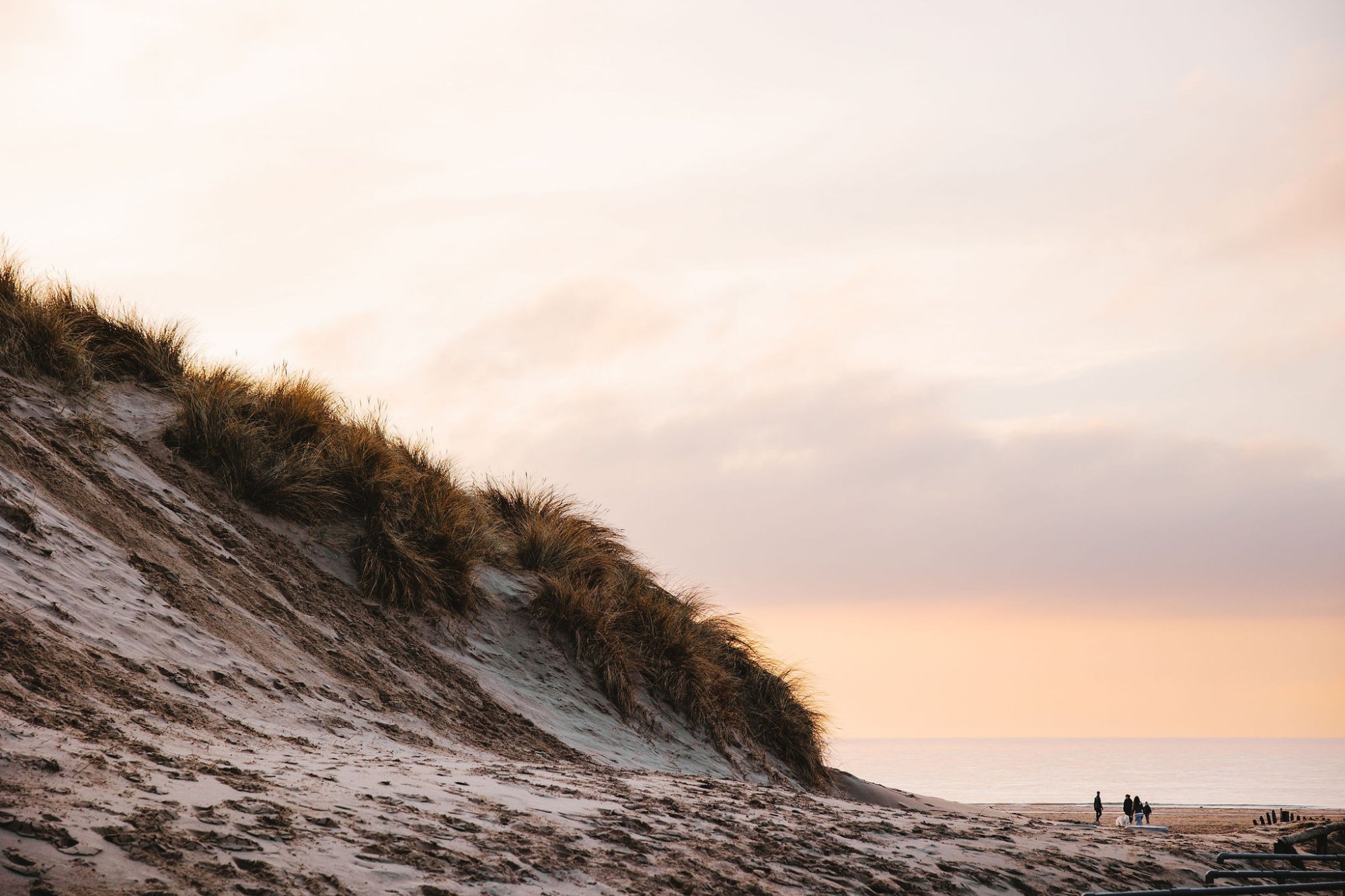 Wandelaars tussen de duinen en het strand bij zonsondergang.