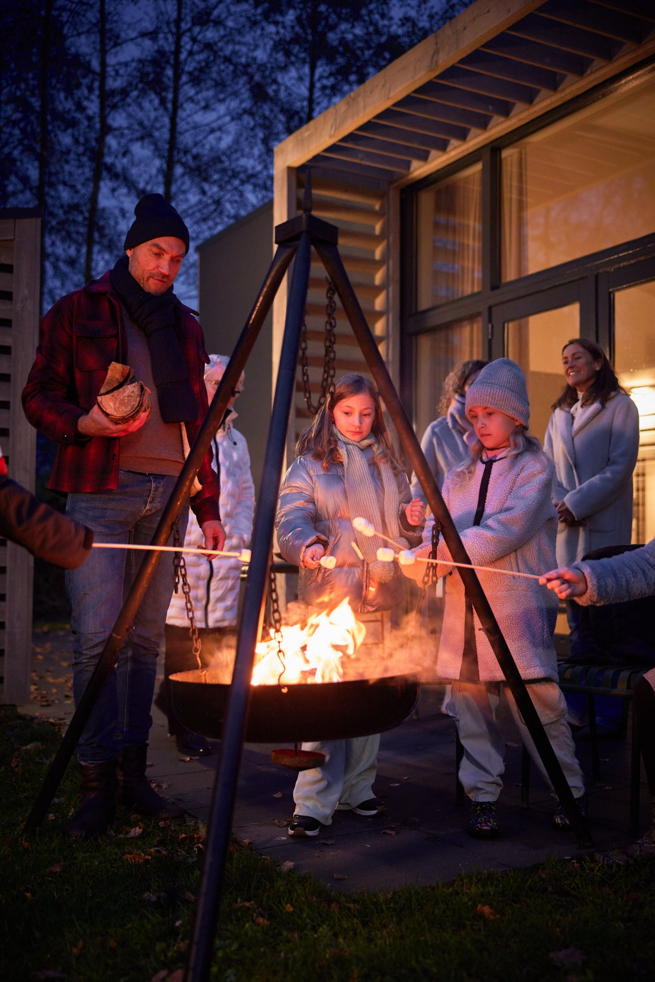 Familie roostert marshmallows bij een vuurkorf naast een vakantiehuis.