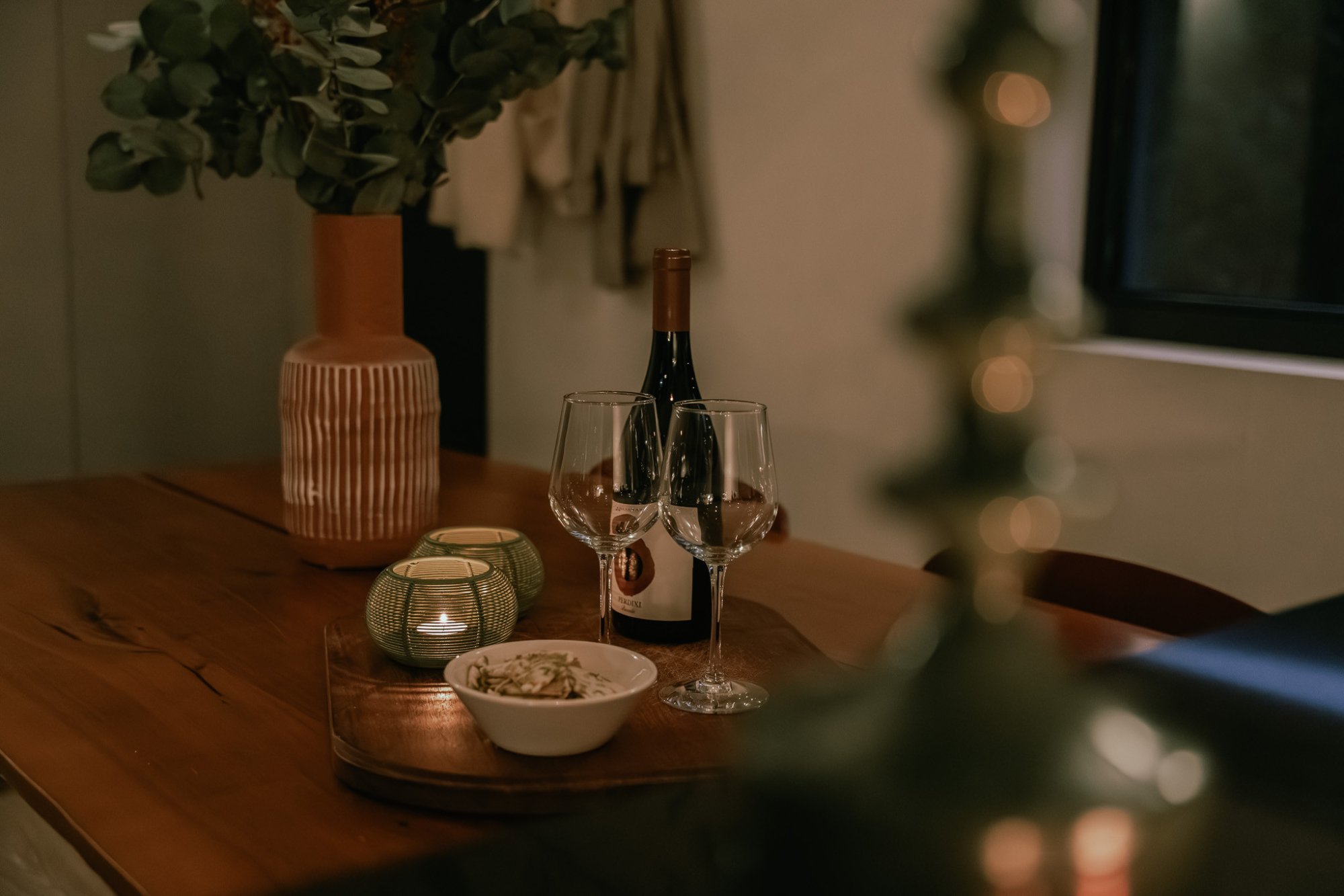 Sfeervol gedekte houten eettafel met wijn, kaarslicht en bloemen.